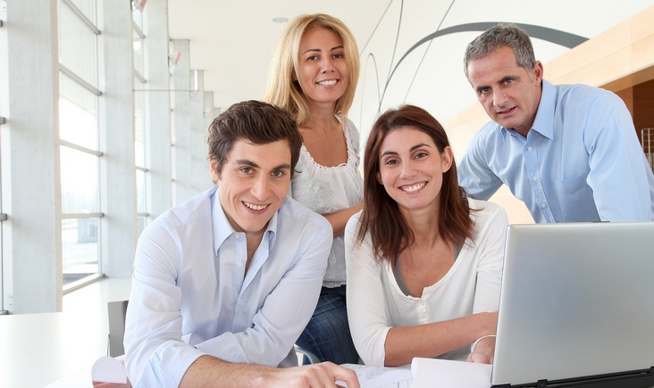 photograph of four professional office workers posed with a laptop computer